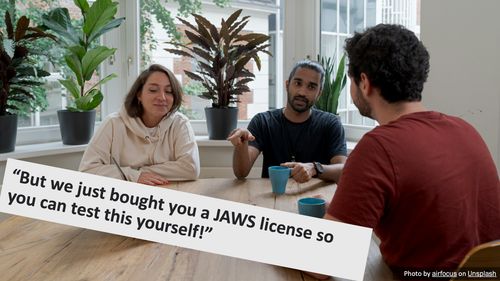 A photograph of three people sat around a table, looking at a laptop in a small conference room with a lot of plants. The overlaid text reads "But we just bought you a JAWS license, so you can test this yourself". There is a photo credit to airfocus on Unsplash.