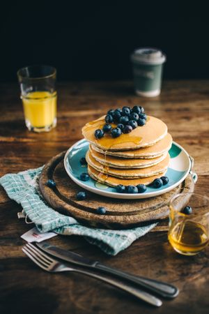 A stock photograph of American-style pancakes alongside some blueberries, orange juice and a cloth napkin